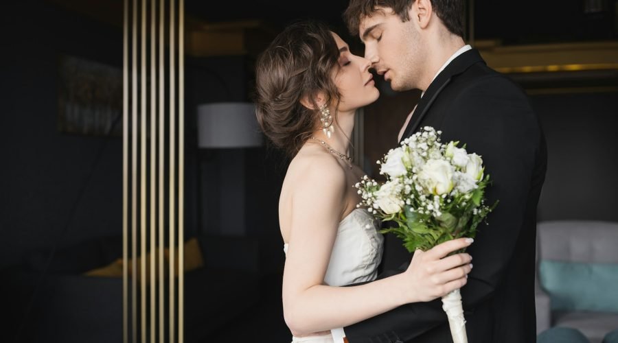side-view-of-good-looking-groom-in-black-formal-wear-kissing-brunette-bride-in-elegant-wedding.jpg